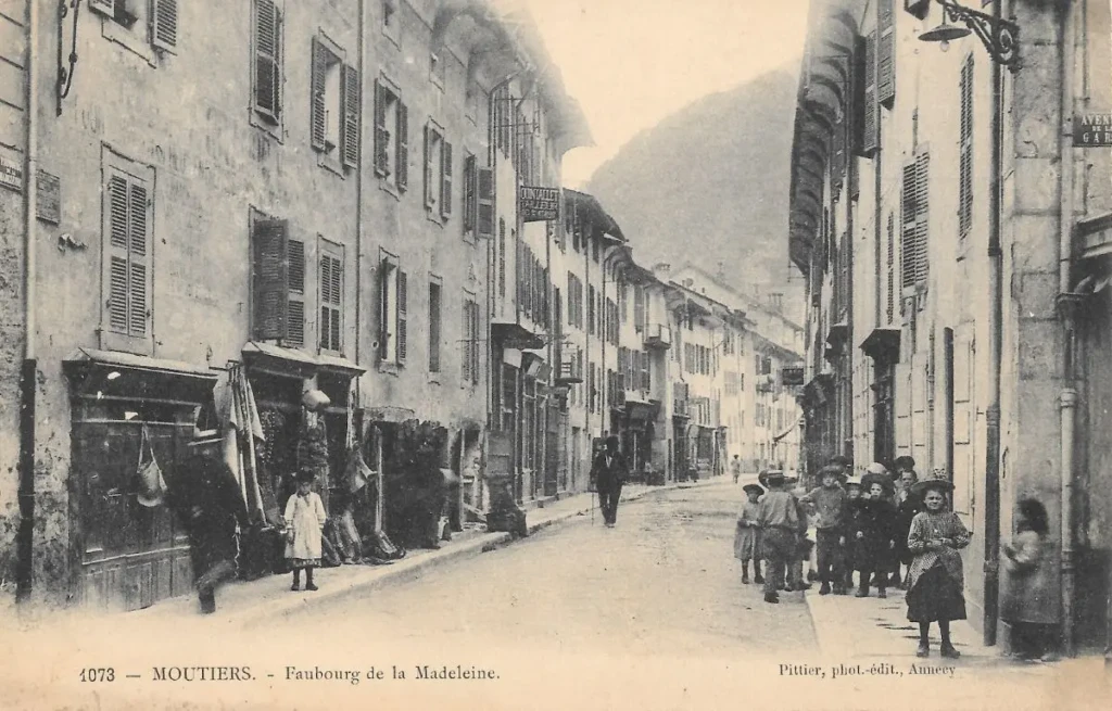 Carte postale ancienne du faubourg de la Madeleine à Moûtiers, scène de rue en Savoie au début du XXe siècle.